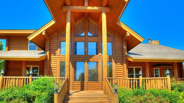 A log cabin with a central entrance, large windows, and a porch with railings. - Naffcation Lodge OKC Cabin And Guest House Retreat On 5 Acres (Oklahoma City)