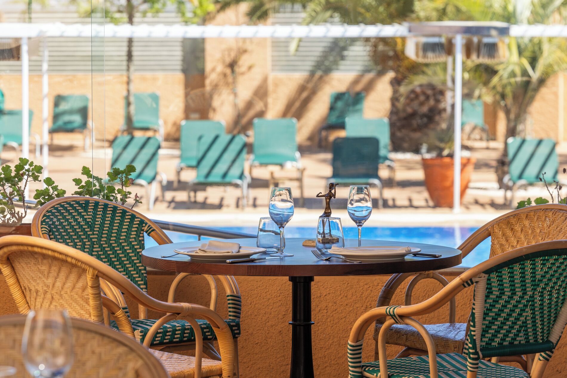 A poolside table with chairs, a statue, and a pool in the background.