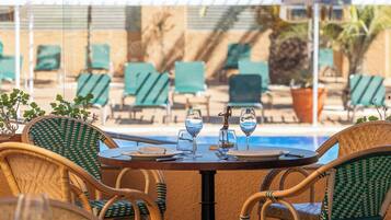 A poolside table with chairs, a statue, and a pool in the background.