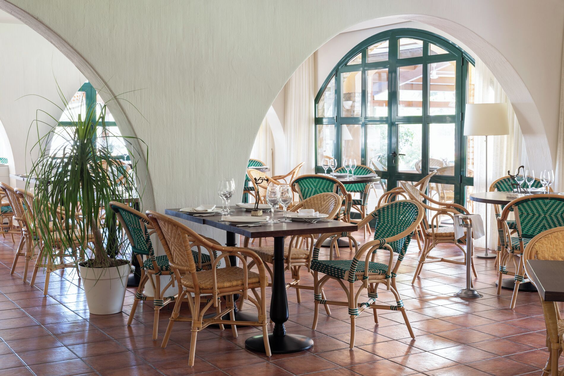 A restaurant interior with high arched ceilings, wicker furniture, and a large window with a view.
