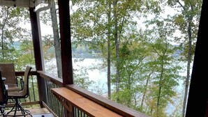 A wooden deck with a railing, several black stools, and a table.