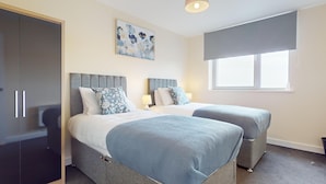 A bedroom with two beds, a wardrobe, a window with blinds, and a painting on the wall. - Basildon - 2 Bed Flat - Sleeps 5 - Near Station (Basildon)