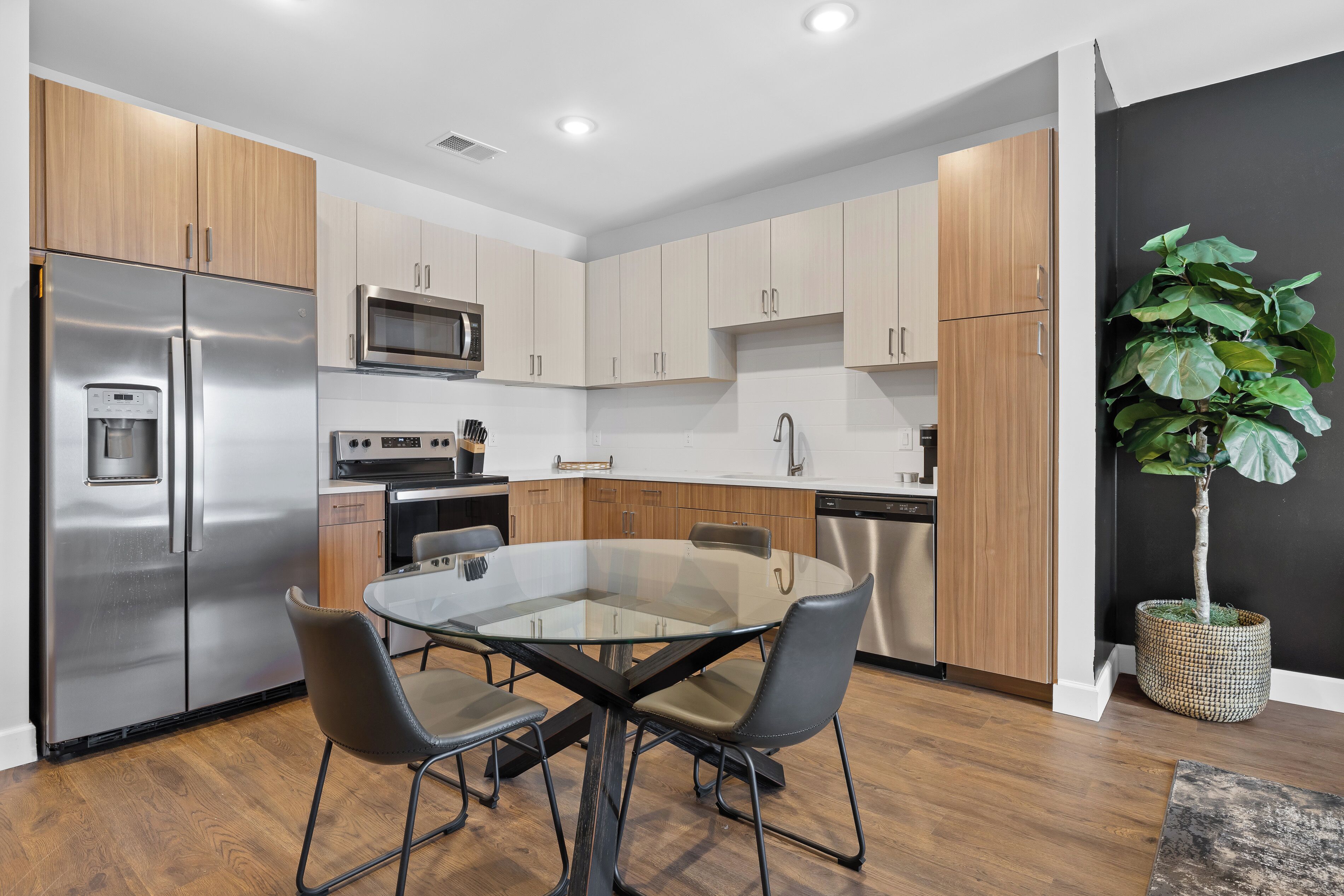A modern kitchen with stainless steel appliances, wooden cabinets, and a glass dining table.