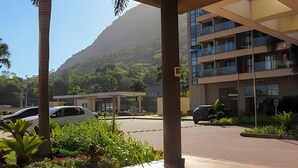 Un bâtiment moderne doté de nombreux balcons, entouré d’une végétation luxuriante et ayant une chaîne de montagnes en toile de fond.