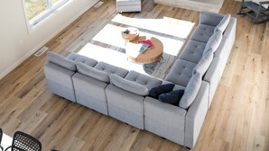 Un salón espacioso con chimenea de piedra, un televisor de pantalla plana grande y un sofá seccional gris.