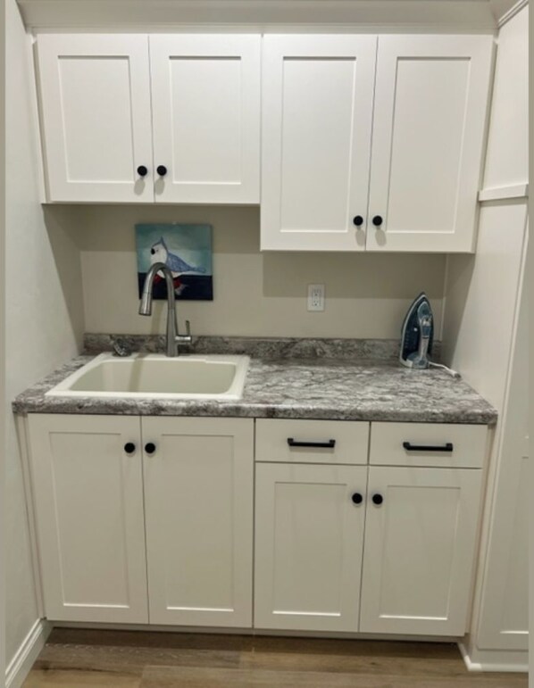 A small kitchen with white cabinets, a granite countertop, a sink, and a painting above the sink.