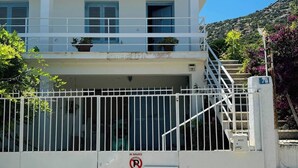 A white building with a gated entrance, a balcony with potted plants, and a no parking sign.