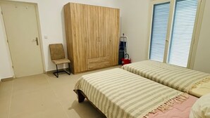 A bedroom with two beds, a wardrobe, a chair, and a window with blinds.