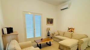 A living room with a sofa, a coffee table, and a lamp. There is a window with blinds, a picture on the wall, and a ceiling light.
