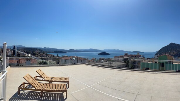 A rooftop terrace with two wooden lounge chairs, a clear view of the sea, and distant mountains.