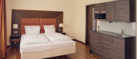 A hotel room with a bed, bedside tables, a built-in kitchen with cabinets and a microwave.