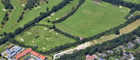 An aerial view of a golf course with multiple greens, sand bunkers, and a clubhouse with a red roof.