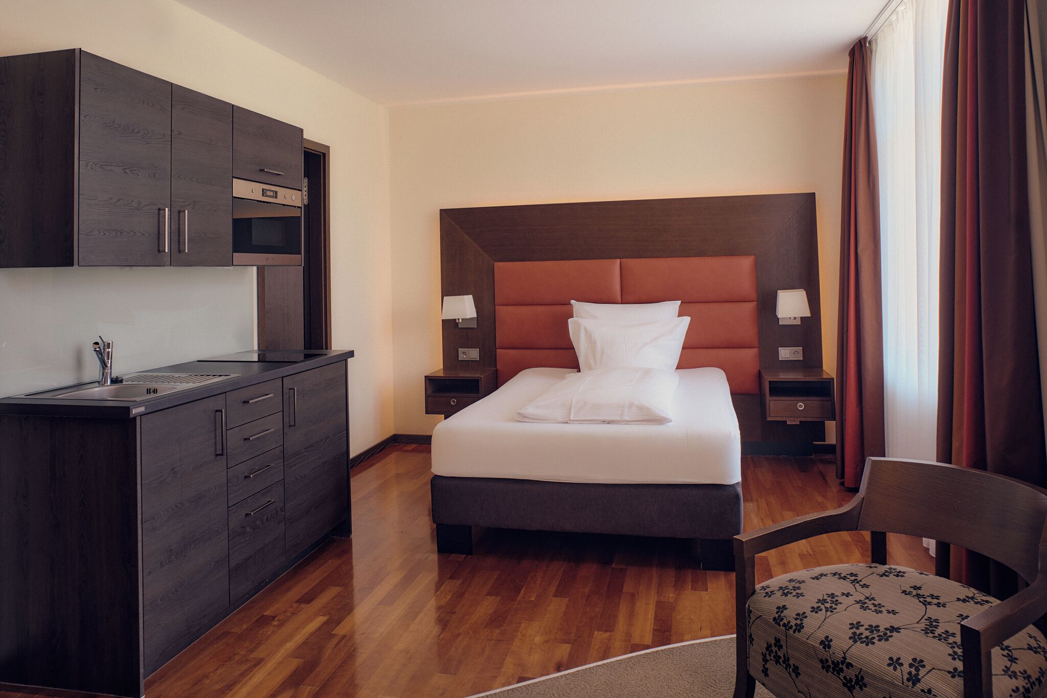 A hotel room with a bed, a desk, a chair, a nightstand, and a wardrobe.