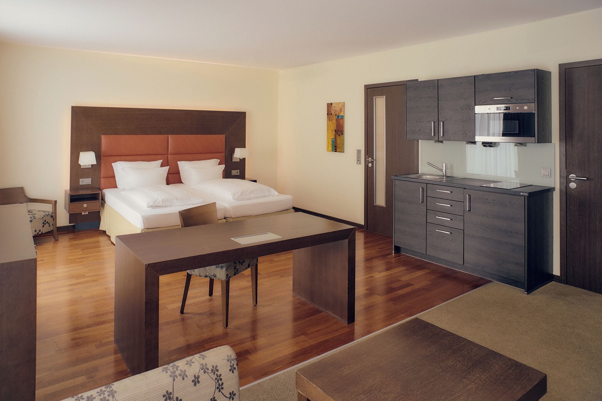 A hotel room with a bed, a desk, a kitchenette, and a bathroom.
