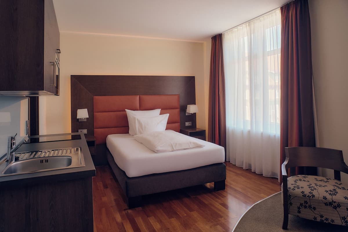 A hotel room with a bed, a desk with a sink, a chair, and a window with curtains.
