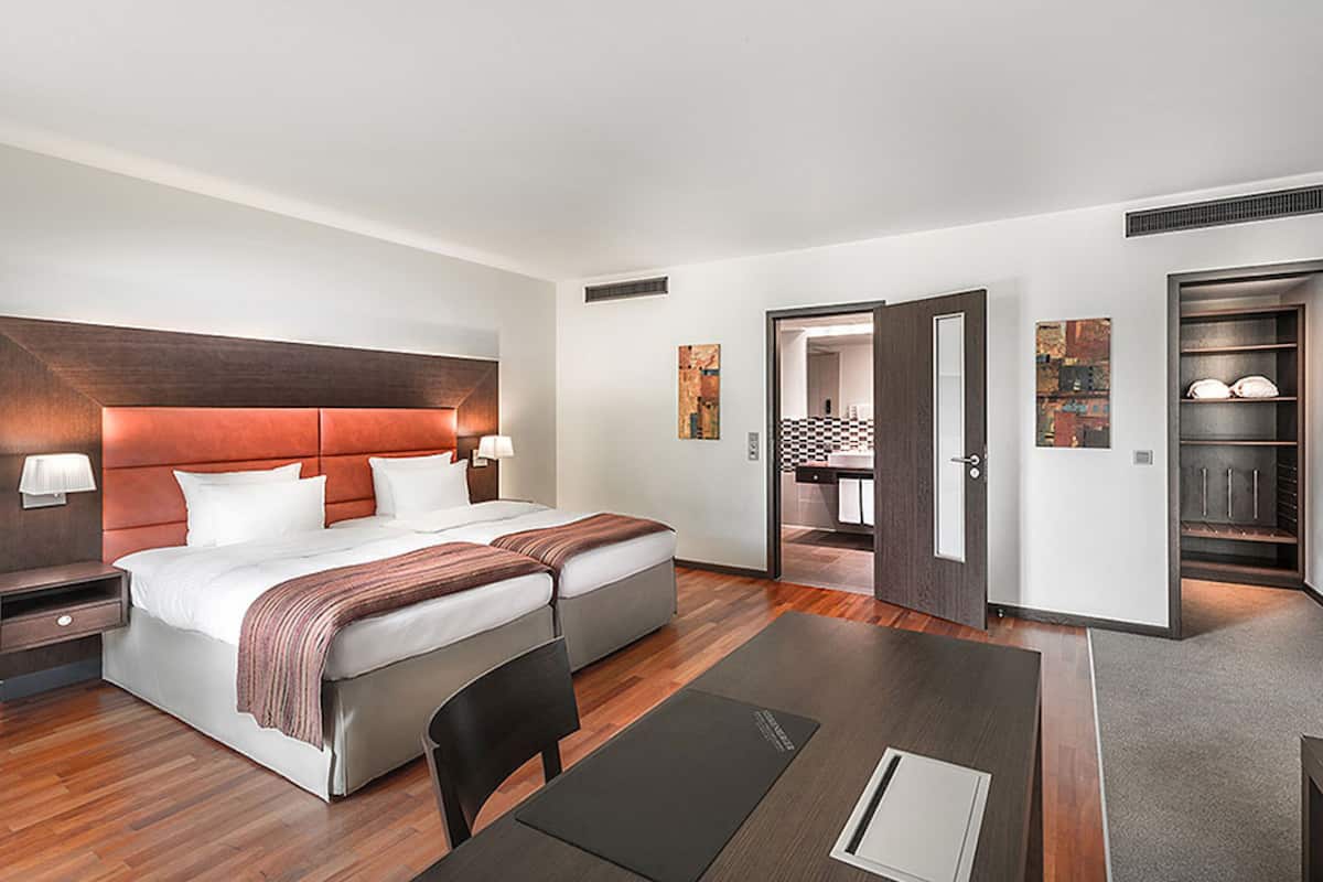 A modern hotel room with a large bed, a desk, a chair, and a walk-in closet.