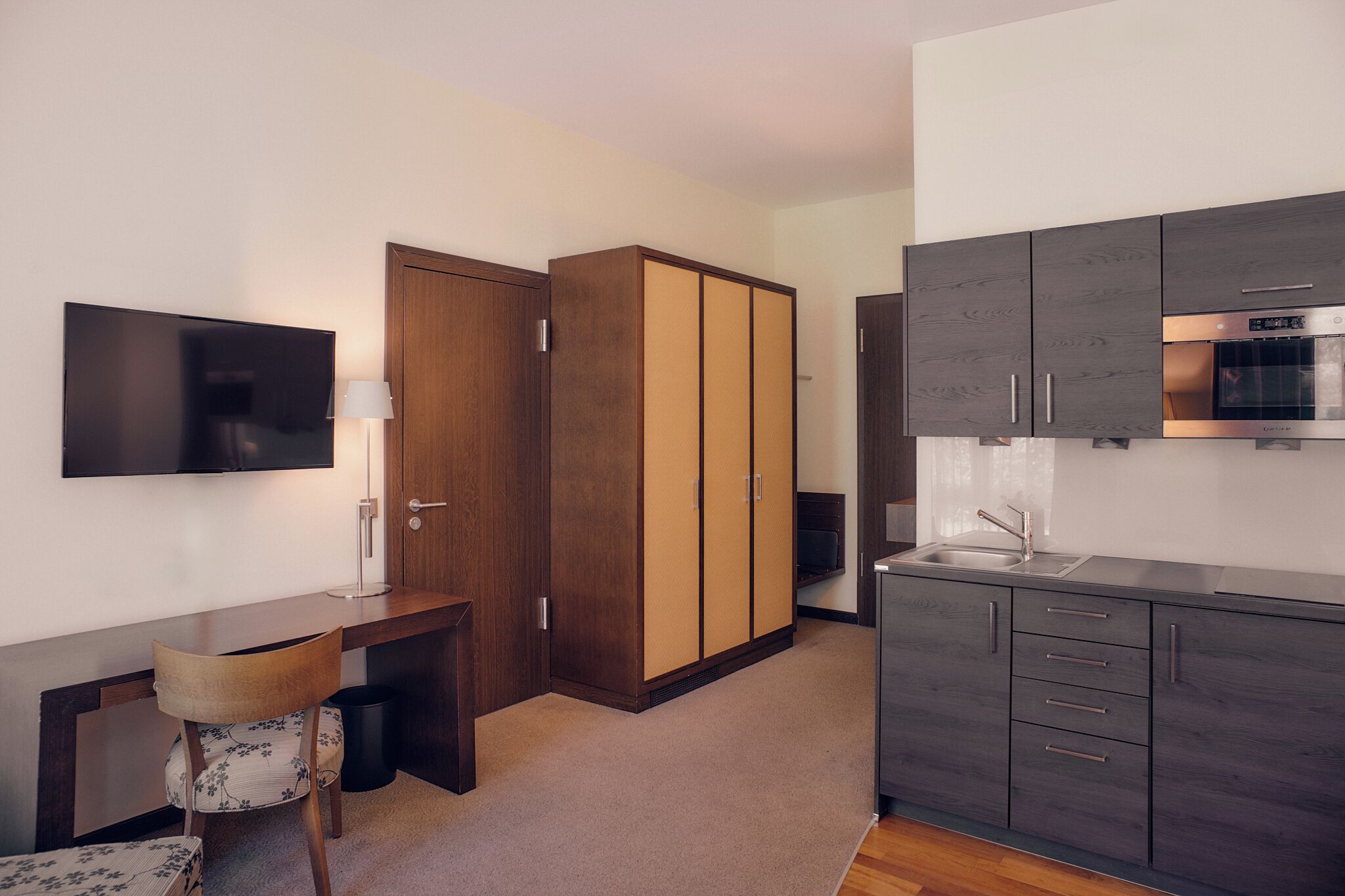 A compact kitchen with a built-in oven, a sink, and a flat-screen TV mounted on the wall.