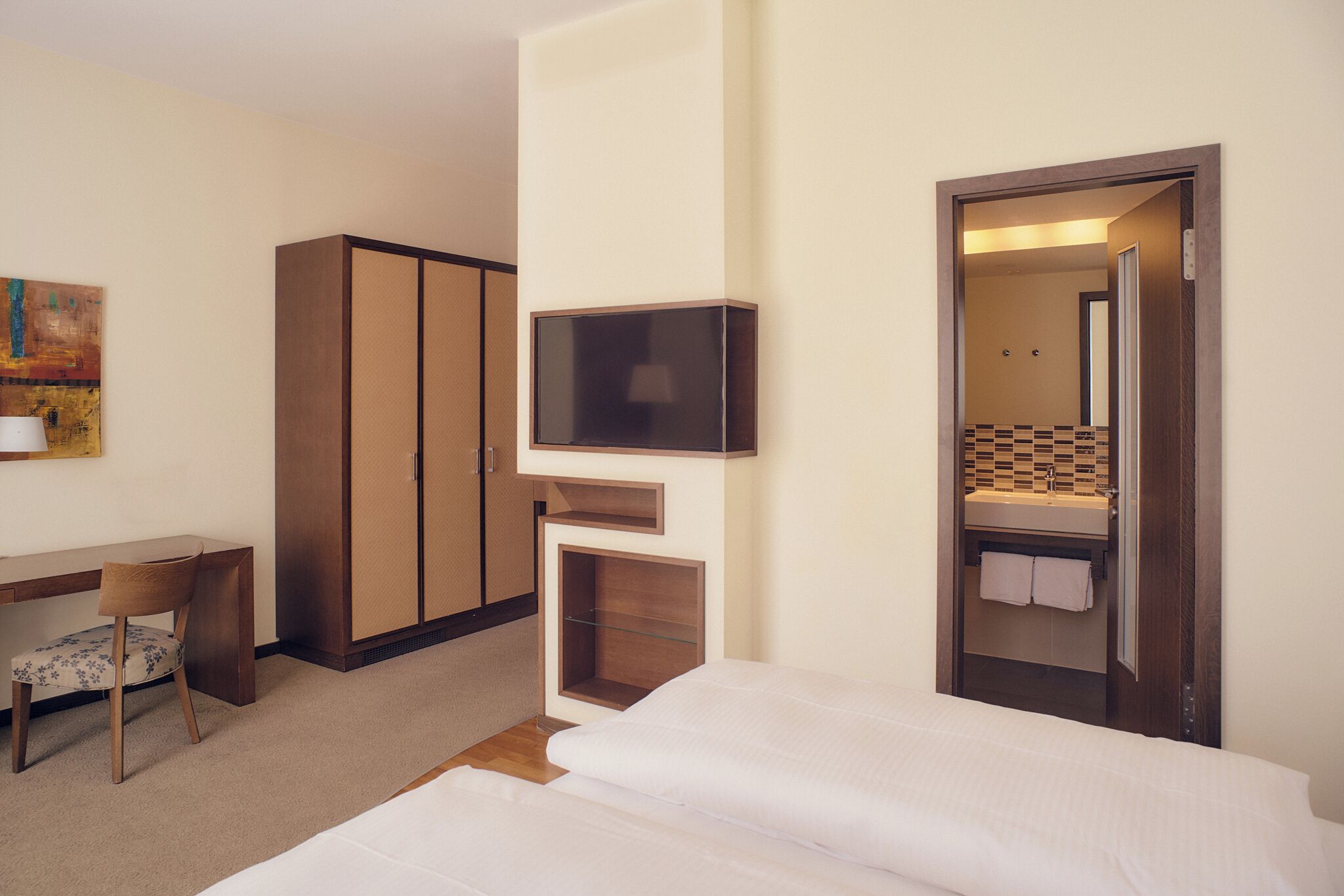 Ein Hotelzimmer mit einem Bett, einem Schreibtisch mit Stuhl, einem Fernseher und einem durchgegangenen Badezimmer.