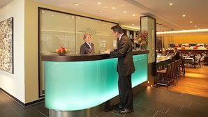 A reception desk with a glass partition, a fruit bowl, and a bar area with seating.