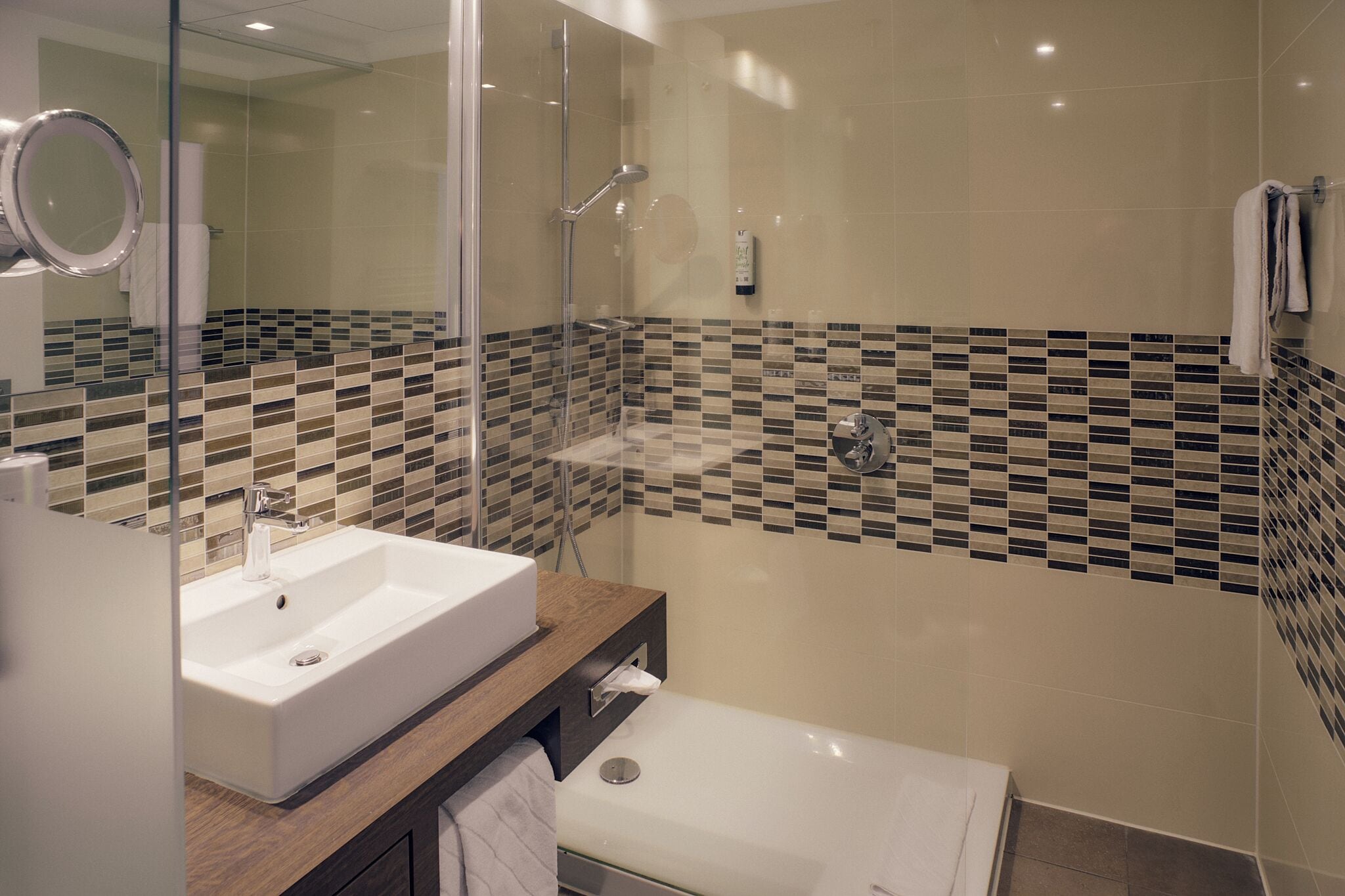 A modern bathroom with a white sink, a glass-enclosed shower, and a tiled backsplash.