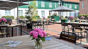 An outdoor seating area with tables and chairs, umbrellas, and a vase of flowers.