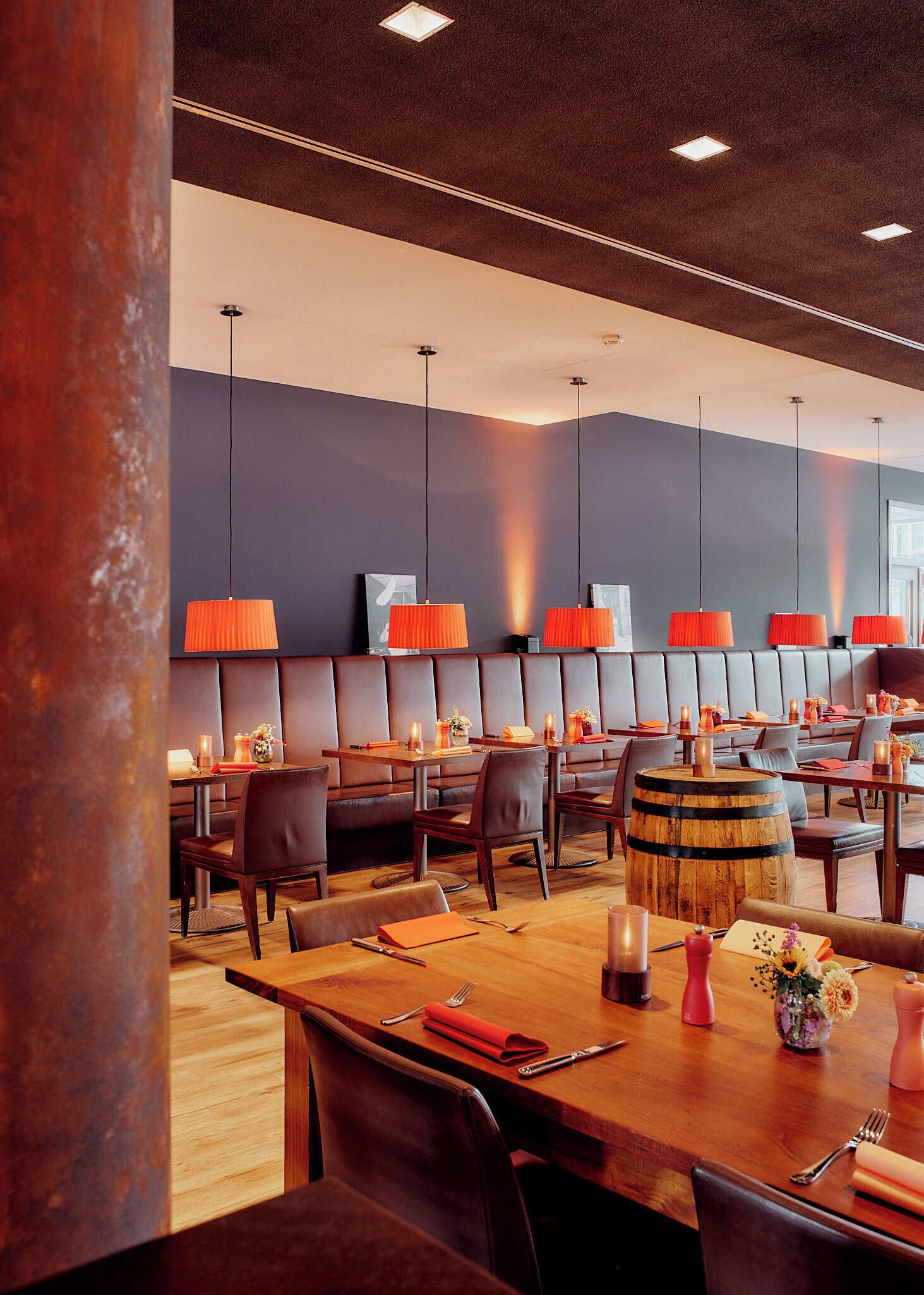 Moderni ravintola, jossa on nahkaverhoillut istuinalueet, puupöydät ja oranssit riippuvalaisimet.