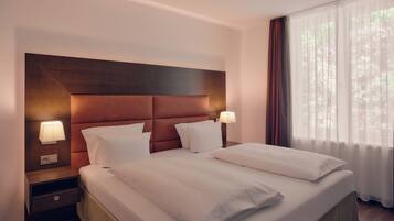 Een hotelkamer met een groot bed, twee nachtkastjes en een raam met dunne gordijnen.