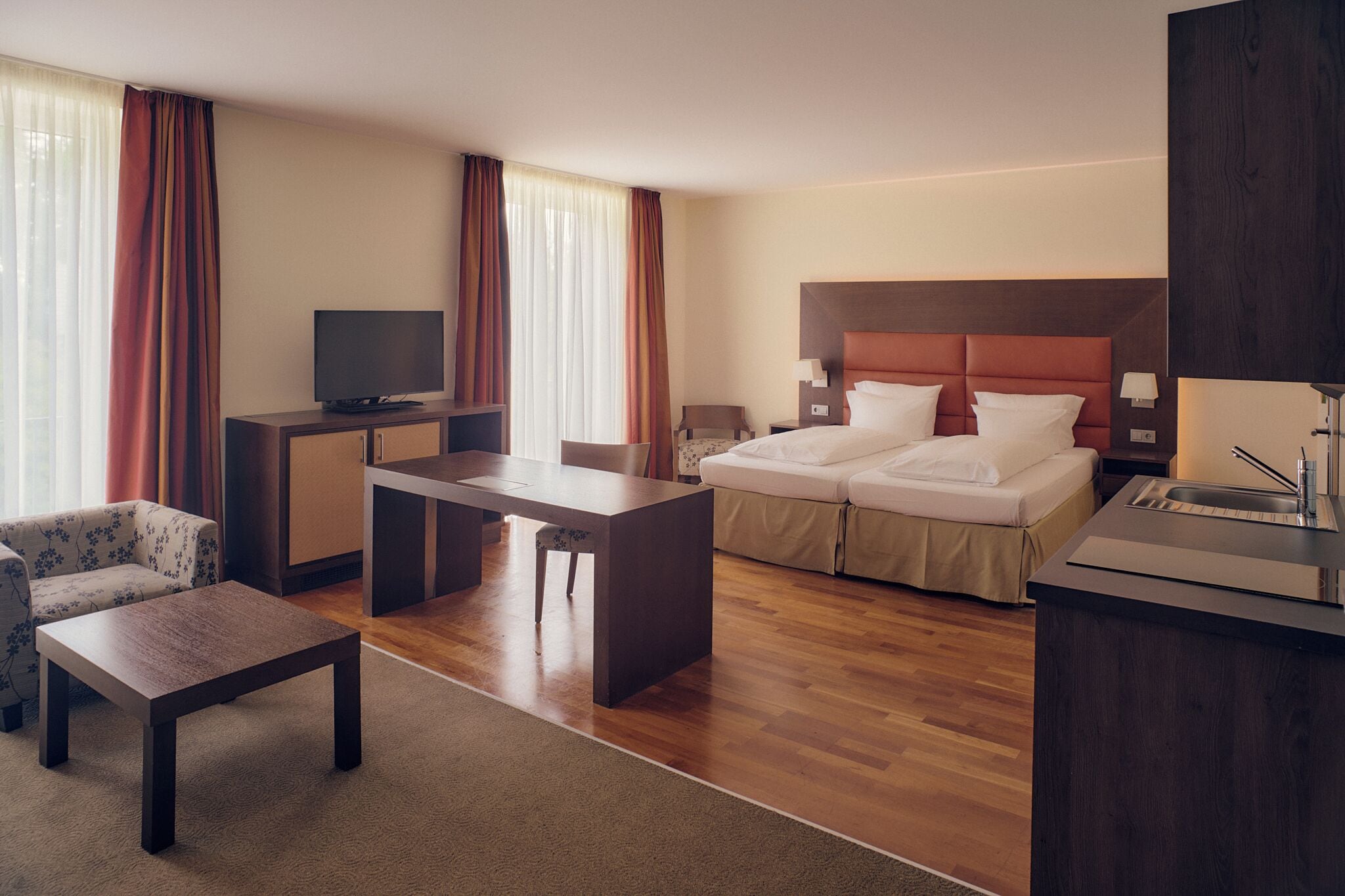 Ein Hotelzimmer mit Bett, Schreibtisch, Fernseher, einer Couch und einer kleinen Küchenzeile.