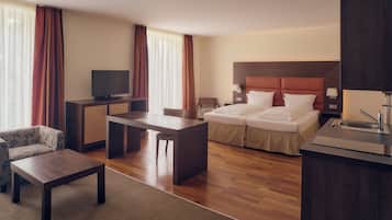 Ein Hotelzimmer mit Bett, Schreibtisch, Fernseher, einer Couch und einer kleinen Küchenzeile.