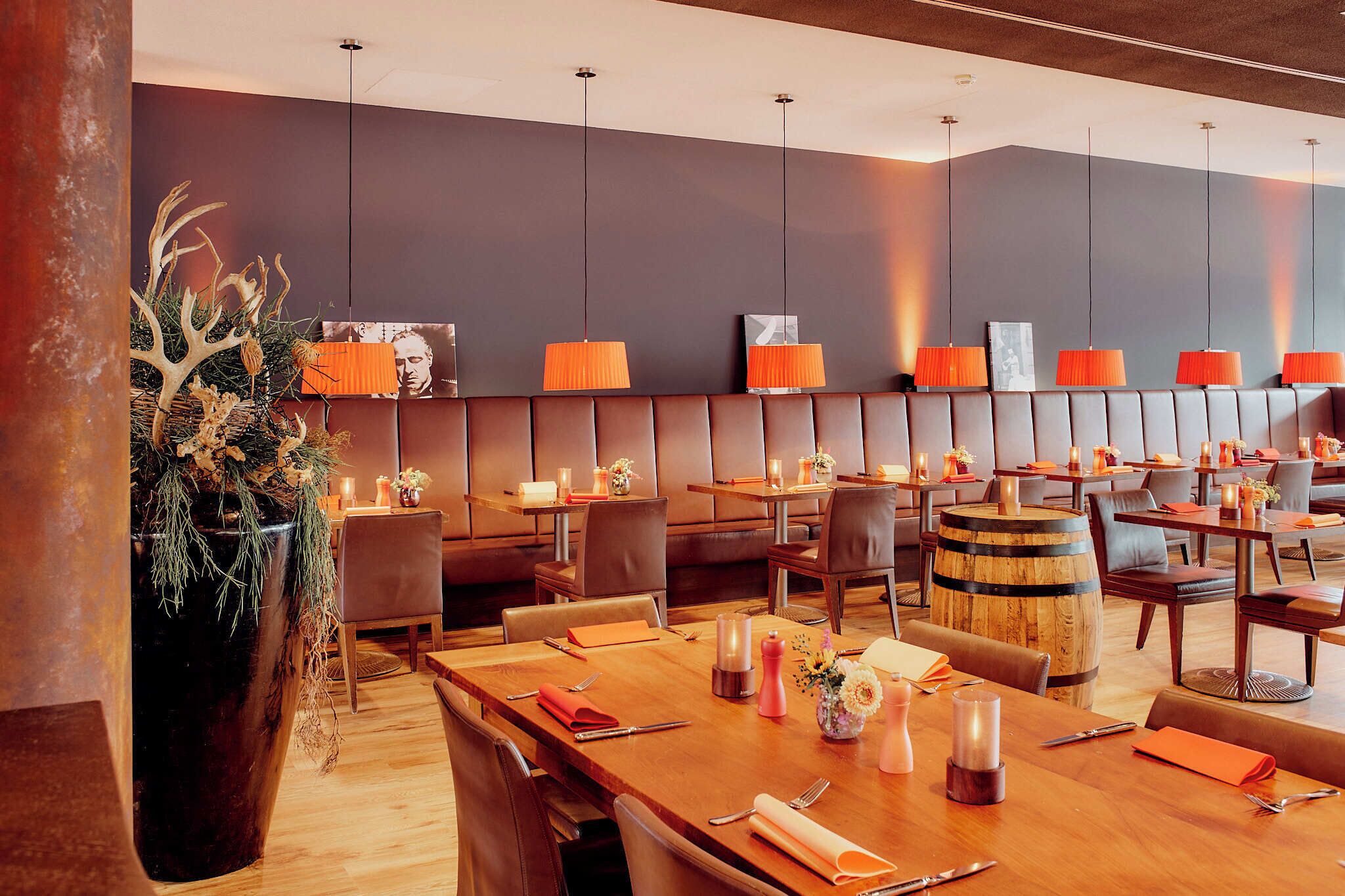 A restaurant with multiple tables, leather booths, and orange pendant lights.