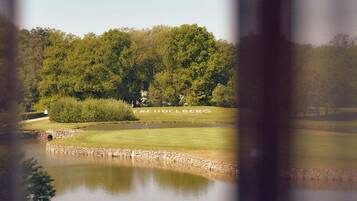 Vista de un campo de golf con un estanque, rodeado de árboles y un puente de piedra.