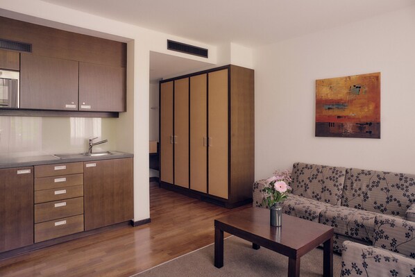 A modern kitchen with wooden cabinets and a dining area with a sofa and a table. - Aparthotel am Golfclub Treudelberg (Hamburg)