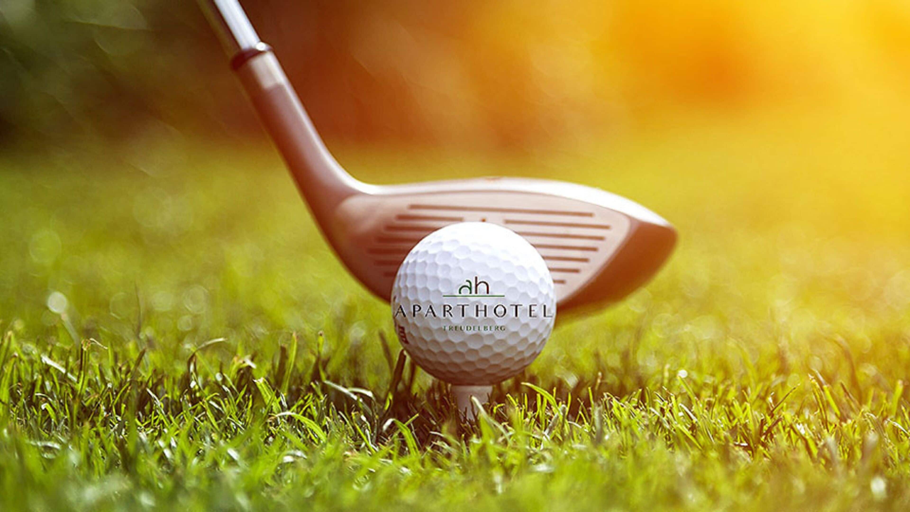 A golf ball with "APARTHOTEL" and "TREUDELBERG" text on it, placed on grass.