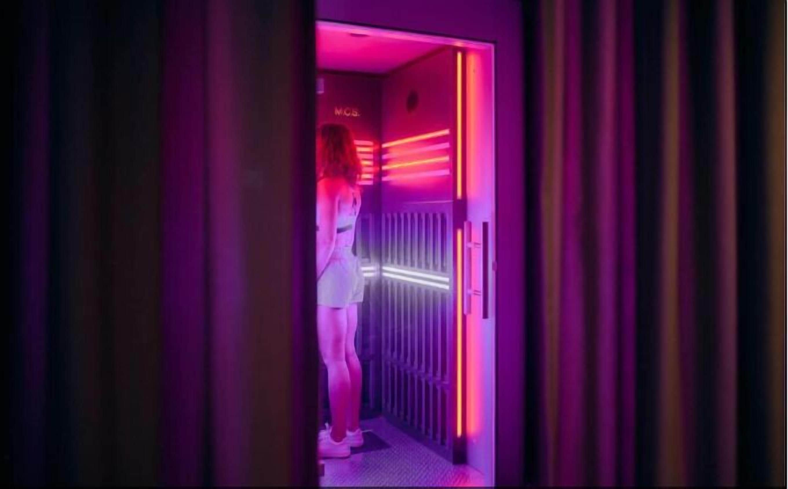 A woman in a white dress standing in a hallway with purple lighting.