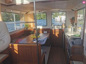 Un interior de barco compacto con comedor, pequeña cocina y zona de estar.