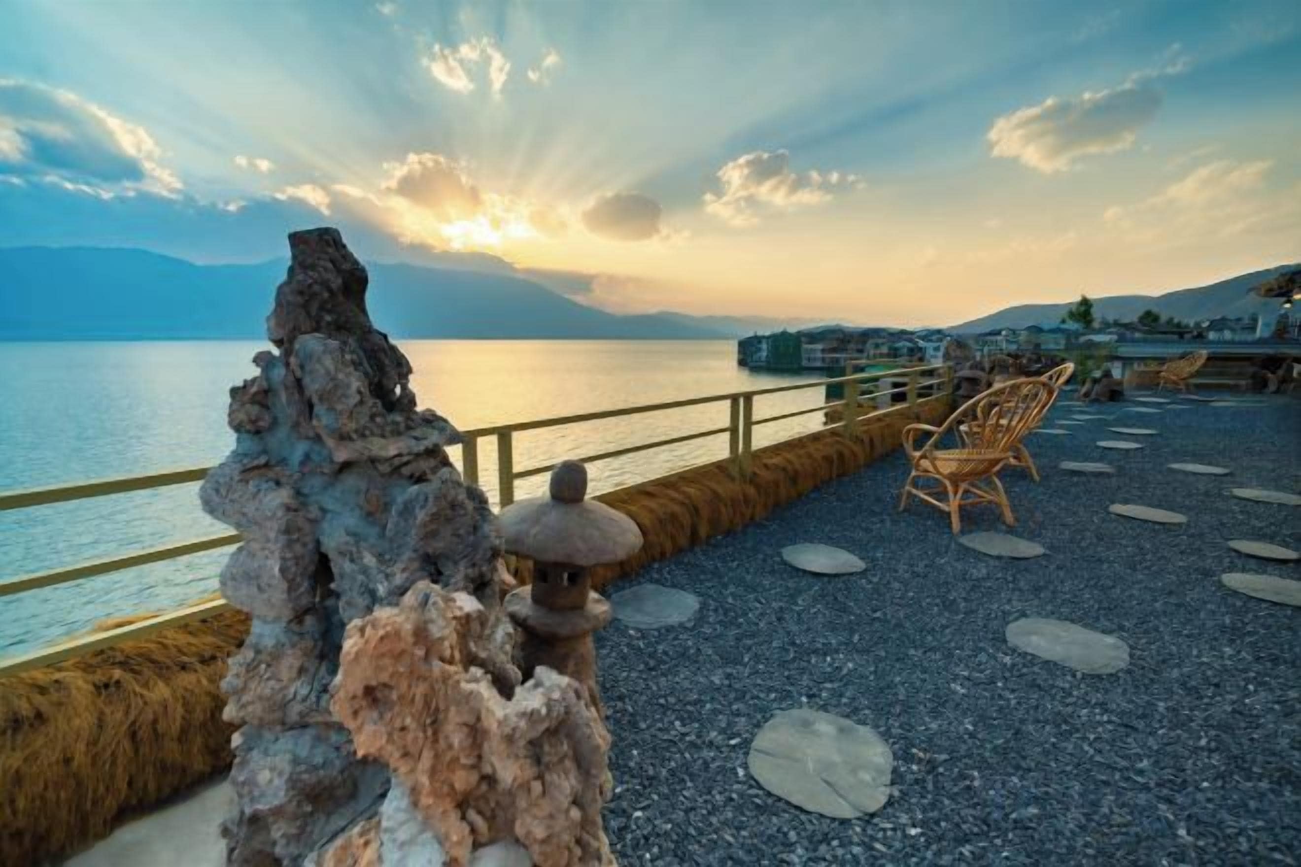 Una terraza con piedras, un farol de piedra, una silla de madera y vista al agua.