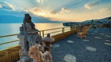 Una terraza con piedras, un farol de piedra, una silla de madera y vista al agua.