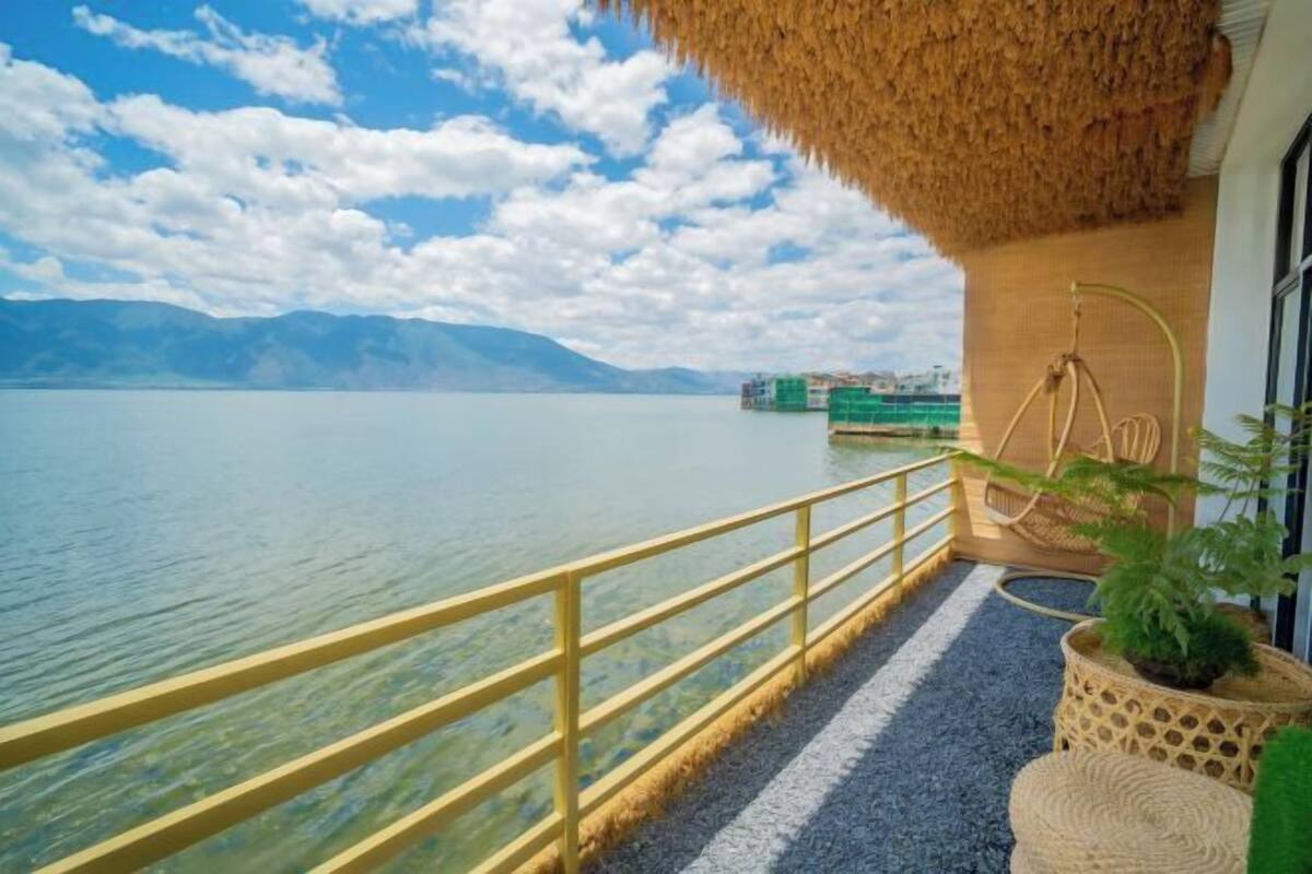 Un balcón con techo de paja que da a un lago tranquilo y montañas lejanas.