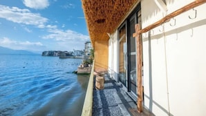 Ein Küstengebäude mit einem Strohdach, einer Steinsitzbank und Blick auf das Meer sowie entfernte Gebäude.