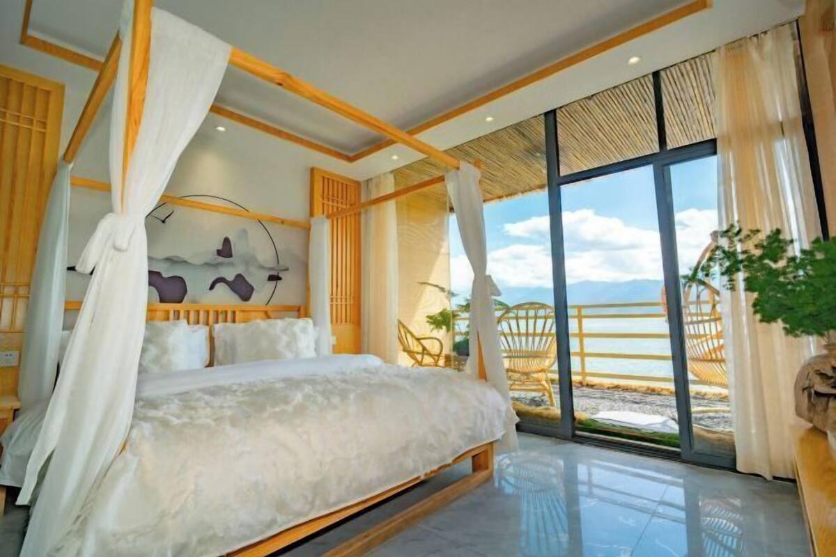 Un dormitorio con una cama grande, vista a la playa y un balcón con mobiliario de mimbre.