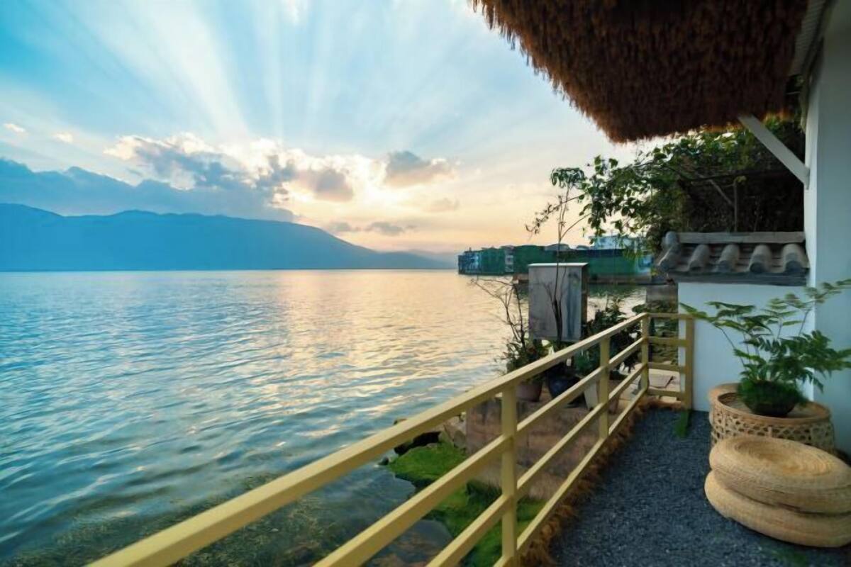 Un balcón con vistas a un lago tranquilo, techo de paja y barandilla.