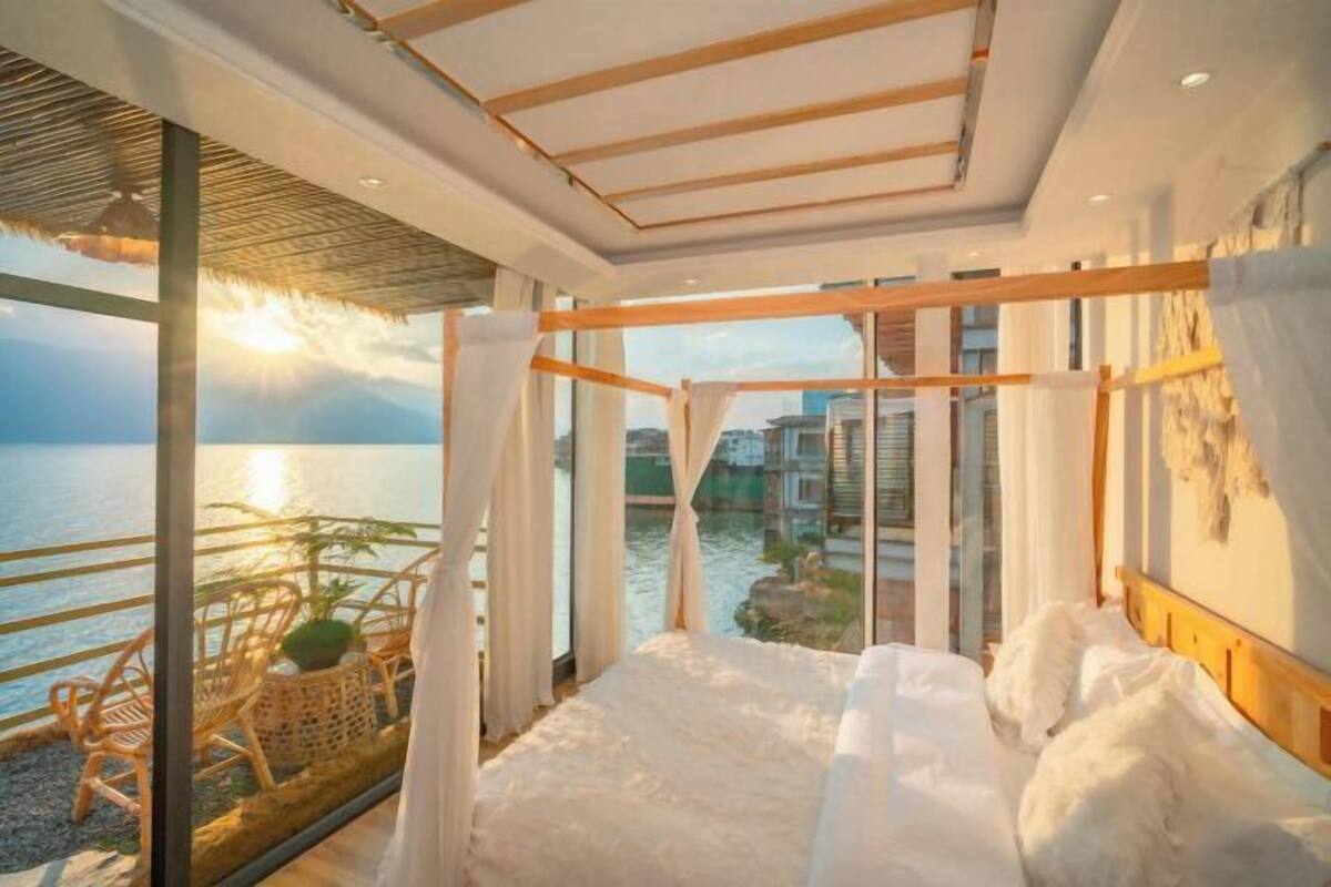 Un dormitorio moderno con una cama grande, vistas al mar y un balcón con sillas de mimbre.