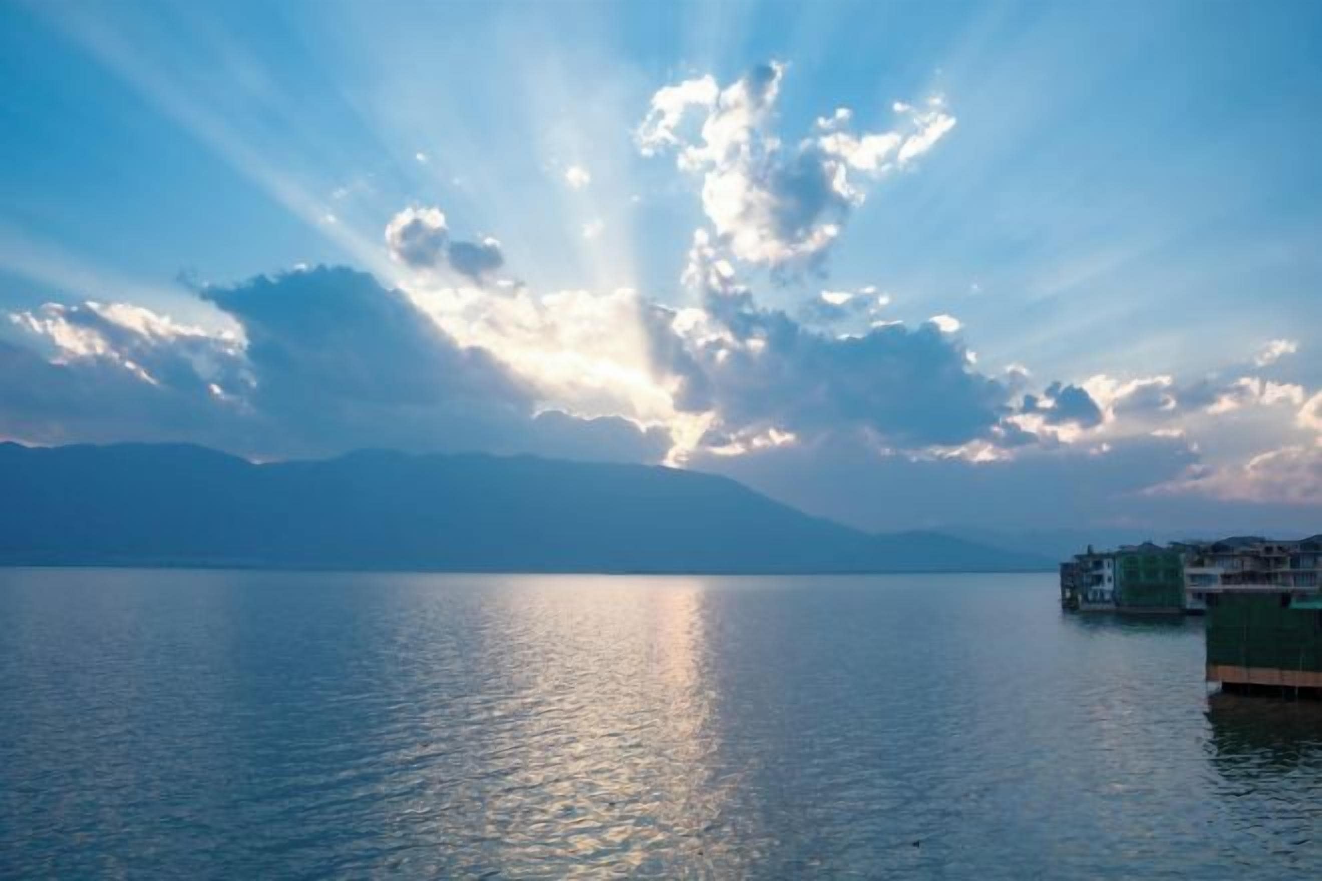 Un lago tranquilo con una cadena montañosa distante y un edificio a la derecha.