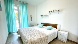 Een slaapkamer met een bed, nachtkastje, stoel en een raam met gordijnen.