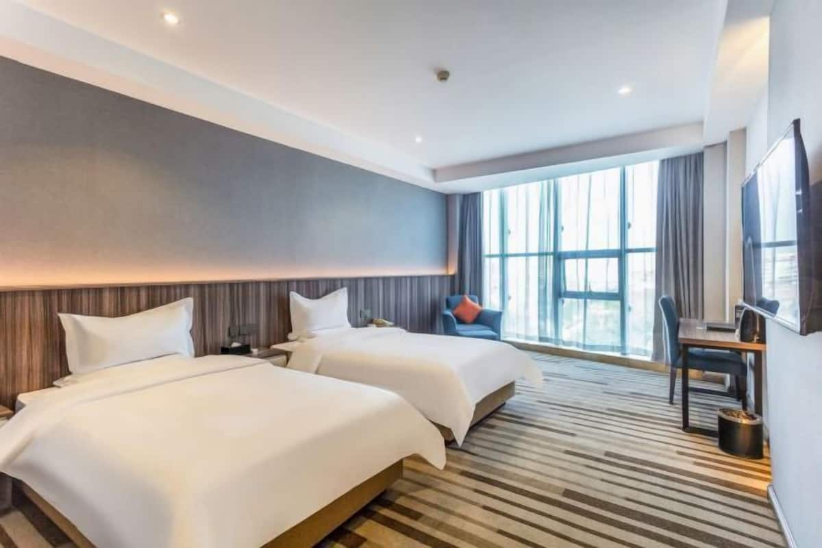 Habitación de hotel con dos camas, un escritorio, una silla y un ventanal grande.