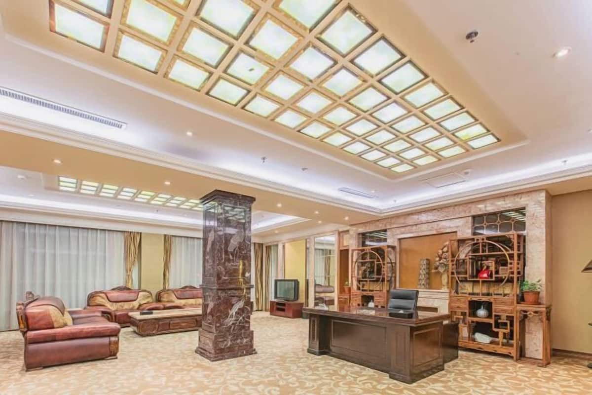 Un hallo de hotel amplio con techo alto, un pilar central grande, un mostrador de recepción y una zona de estar con sofás.