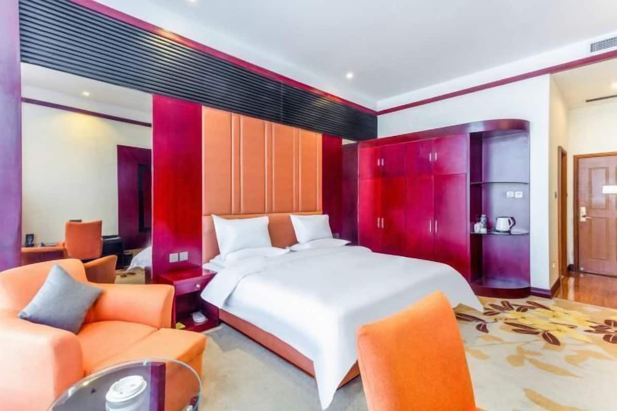 Una habitación de hotel con cama, sillas anaranjadas, armario y cafetera.