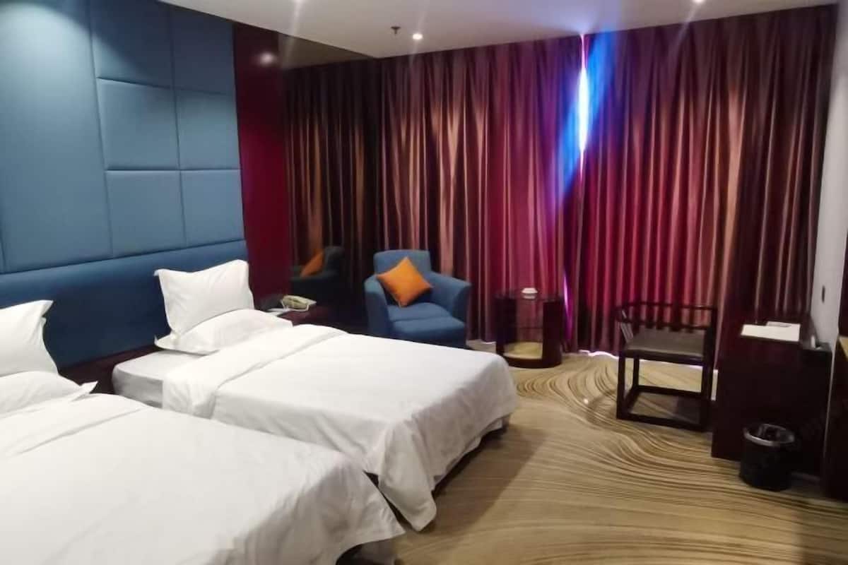Habitación de hotel con dos camas, un sillón azul, una mesita y un escritorio con una silla.