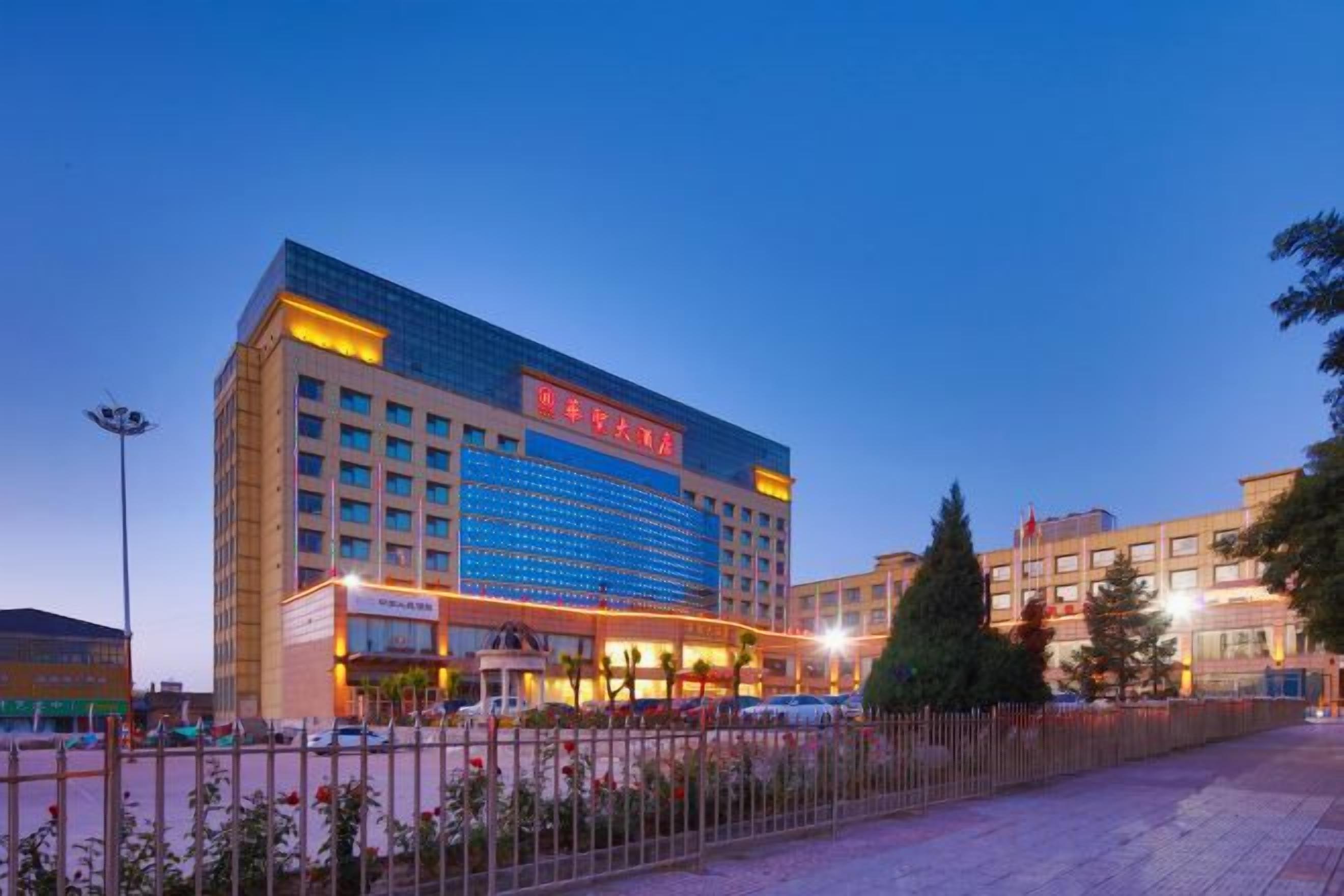 A large hotel with multiple floors, a prominent sign, and a fenced outdoor area with flowers.