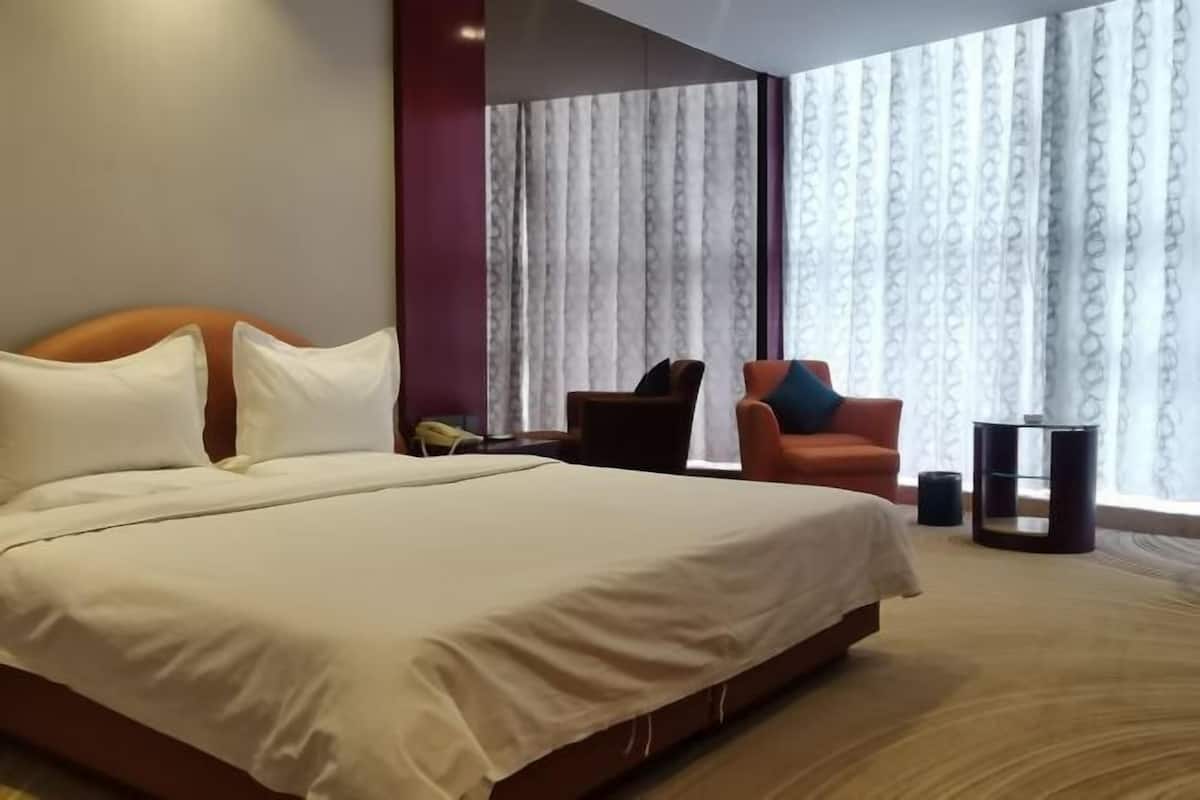 Habitación de hotel con una cama grande, una silla, una mesita y un ventanal con cortinas.